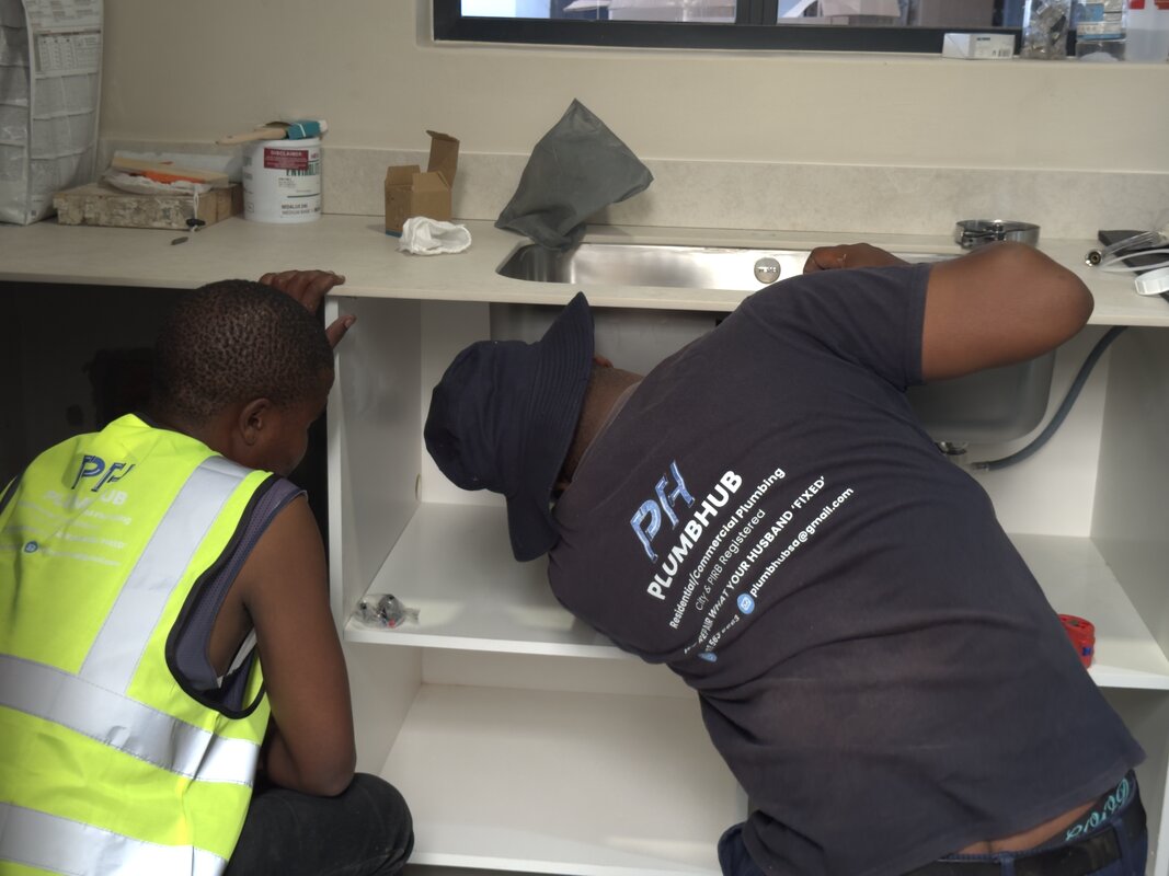 Two Plumbhub plumbers repairing the pipes under a sink
